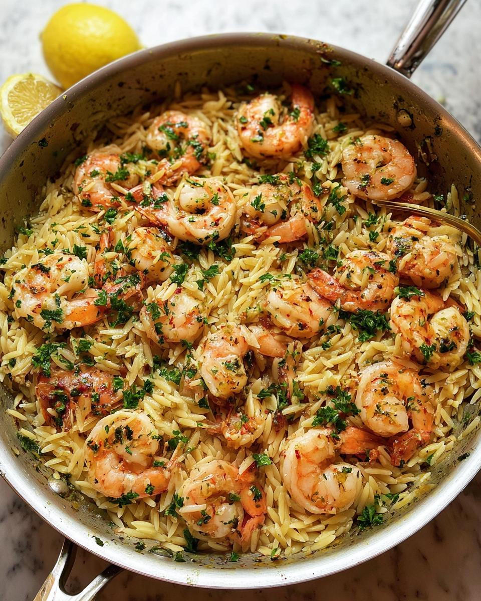 Overhead shot of Garlic-Butter Shrimp & Orzo in a skillet, garnished with parsley and served with lemon.