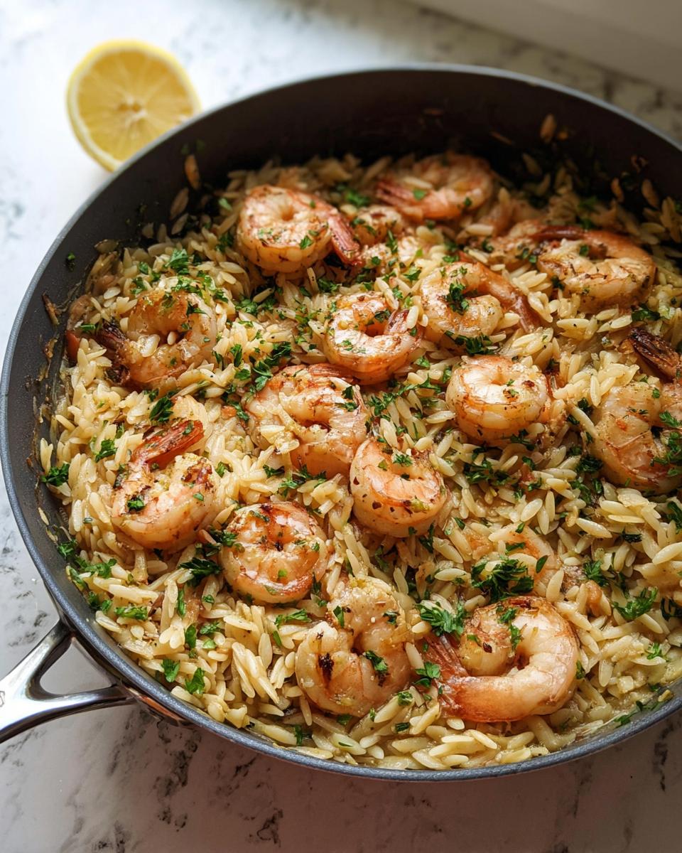 Overhead shot of Garlic-Butter Shrimp & Orzo in a pan, garnished with parsley and a lemon wedge.