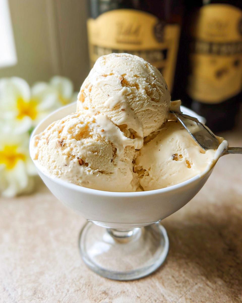 Three scoops of creamy Baileys ice cream in a white bowl, with a spoon digging into the side.
