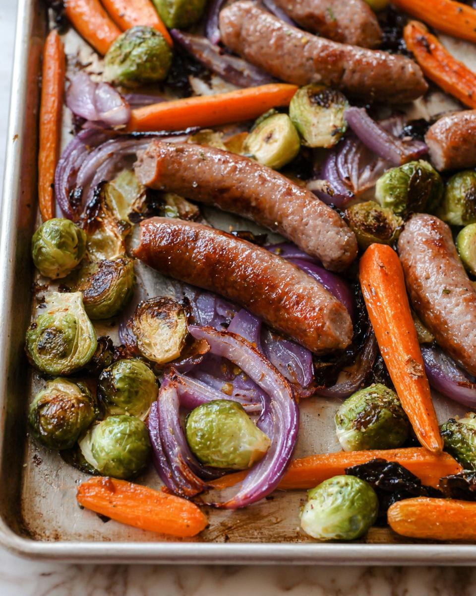 Overhead view of Sheet‑Pan Sausage & Veggies, featuring sausage, carrots, Brussels sprouts, and red onions.