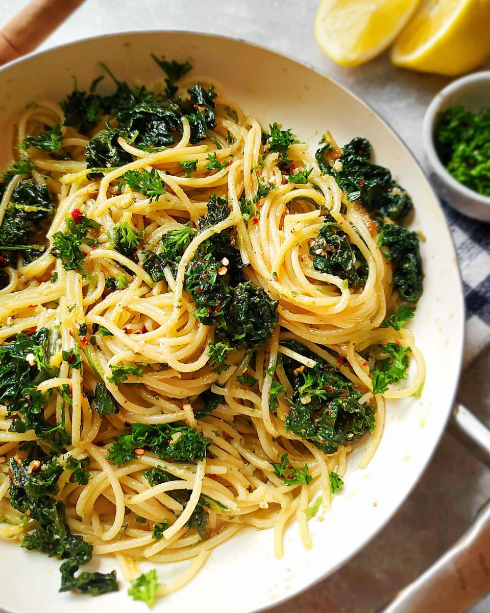 A close-up of Spaghetti Aglio e Olio with wilted kale and fresh parsley, garnished with red pepper flakes.