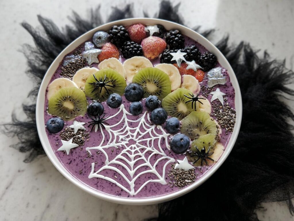 A vibrant Spooky Halloween Smoothie Bowl topped with kiwi, banana, blueberries, blackberries, strawberries, and a white chocolate spiderweb.