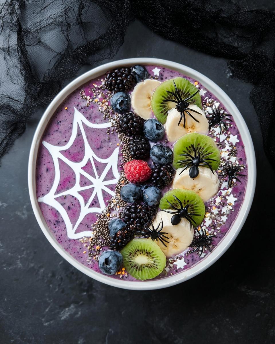 A Spooky Halloween Smoothie Bowl decorated with a white spiderweb, berries, kiwi, banana slices, and plastic spiders.