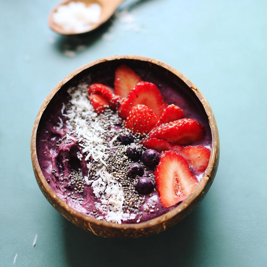 A vibrant Spooky Smoothie Bowl topped with fresh strawberries, blueberries, chia seeds, and coconut flakes in a coconut shell bowl.