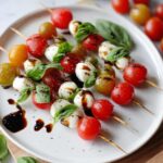 Close-up of several 5-Ingredient Caprese Skewers featuring cherry tomatoes, mozzarella balls, and basil drizzled with balsamic glaze.