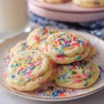A stack of soft, freshly baked Confetti Sprinkle Cookies topped with colorful jimmies on a white plate.