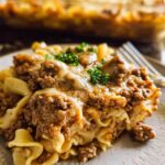 A close-up serving of cheesy Amazing Beef Enchilada Casserole with ground beef and noodles, garnished with parsley.