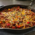 Close-up of Amazing Stuffed Pepper Casserole topped with melted cheddar and herbs in a dark cast iron skillet.