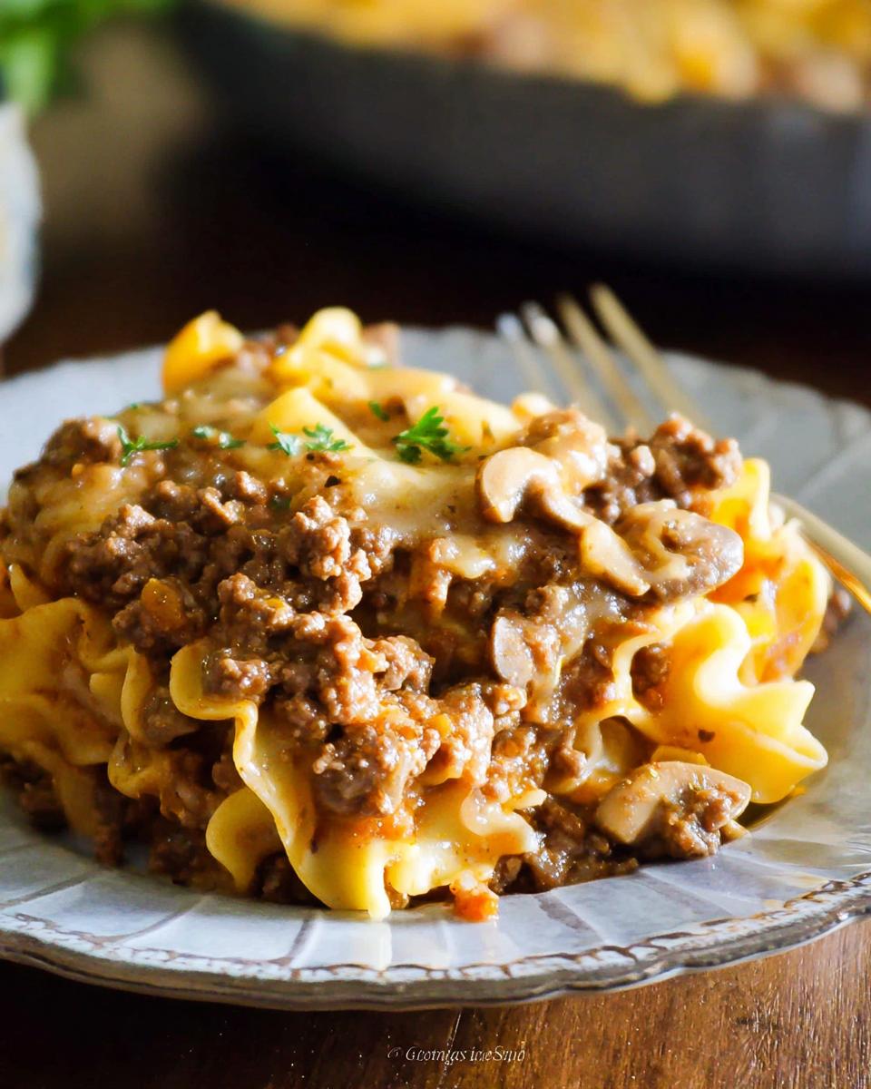 A close-up serving of Beef Enchilada Casserole featuring ground beef, melted cheese, mushrooms, and ruffled pasta on a plate.