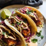 Three delicious Blackened Salmon Tacos filled with crispy fish, red cabbage slaw, and drizzled with creamy sauce.