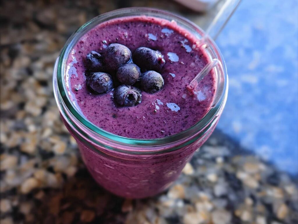 Overhead close-up of a thick, purple Blueberry Oat Breakfast Smoothie topped with frozen blueberries.