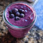 Overhead close-up of a thick, purple Blueberry Oat Breakfast Smoothie topped with frozen blueberries.