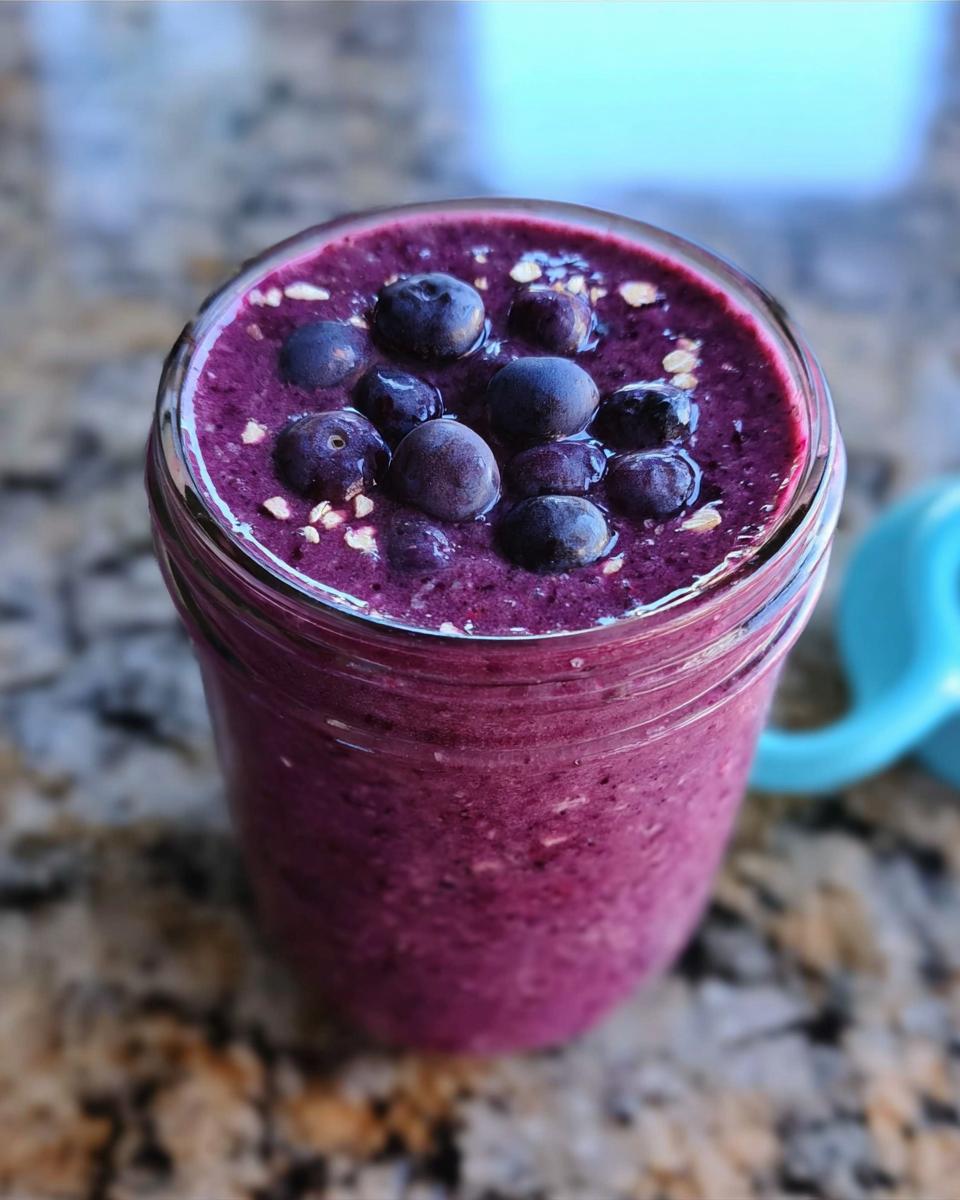 A thick, vibrant purple Blueberry Oat Breakfast Smoothie topped with fresh blueberries and oats in a glass jar.