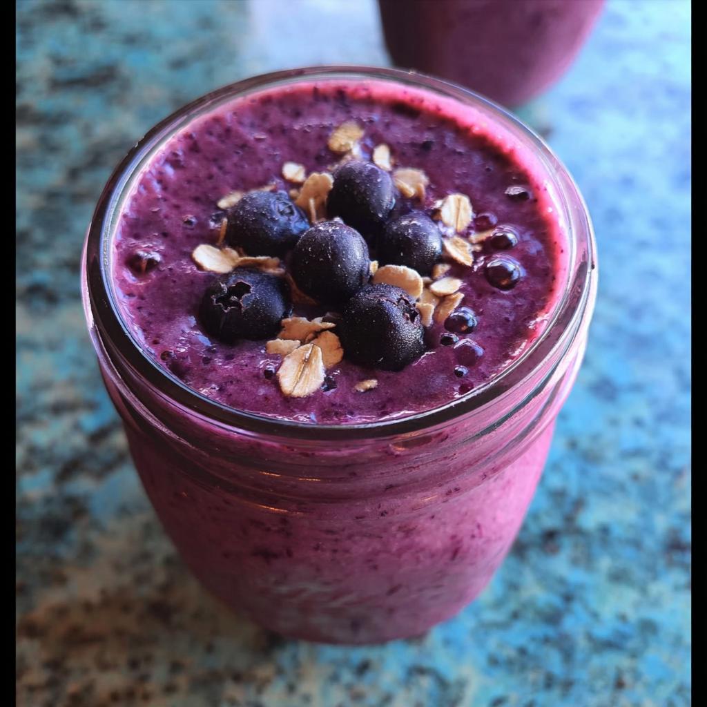 Close-up overhead view of a thick Blueberry Oat Breakfast Smoothie topped with fresh blueberries and rolled oats.