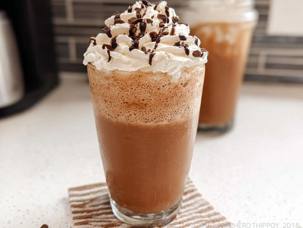 A tall glass filled with a blended Mocha Frappuccino, topped with whipped cream, chocolate syrup, and sprinkles.