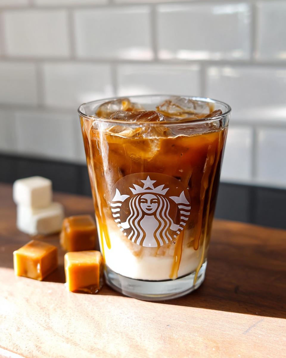 A glass featuring a layered Café-Style Iced Caramel Macchiato copycat drink with caramel drizzle and a Starbucks logo sticker.