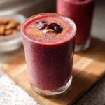 A vibrant, deep red Cherry Almond Smoothie topped with fresh cherries and almond butter.