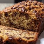 Close-up of a freshly baked Chocolate Chip Banana Bread loaf with one slice cut, showing moist texture and melted chocolate chips.