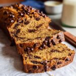 A sliced loaf of moist Healthy Banana Bread (Whole Wheat) studded with chocolate chips, resting on parchment paper.