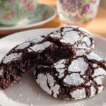 Close-up of rich, dark Chocolate Crinkle Cookies dusted heavily with white powdered sugar on a white plate.