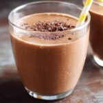 Close-up of a thick Chocolate Peanut Butter Smoothie topped with chocolate shavings and a yellow straw.