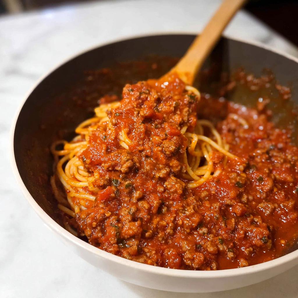 A close-up of Classic Spaghetti with Meat Sauce being served with a wooden spoon from a bowl.