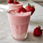 Close-up of a refreshing Strawberry Banana Smoothie garnished with fresh strawberries on a white marble counter.