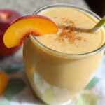 A close-up of a creamy Peach Yogurt Smoothie garnished with a fresh peach slice and cinnamon.