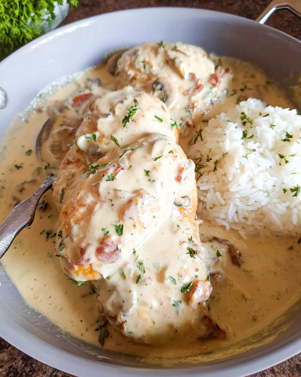 Three pieces of chicken smothered in a thick, creamy sauce with mushrooms and herbs, served next to white rice.
