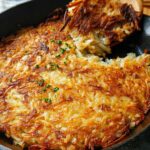 Golden brown, crispy skillet Hash Browns being lifted out of a black cast iron pan with a wooden spatula.