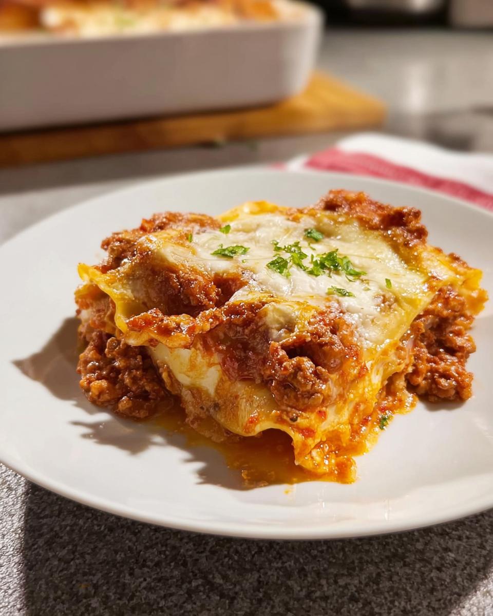 A hearty slice of Easy Lasagna Dinner for Busy Families on a white plate, topped with melted cheese and parsley.