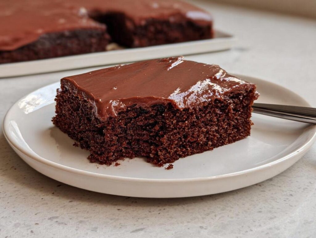 A moist slice of Easy Snacking Sheet Cake with rich, glossy chocolate frosting on a white plate.