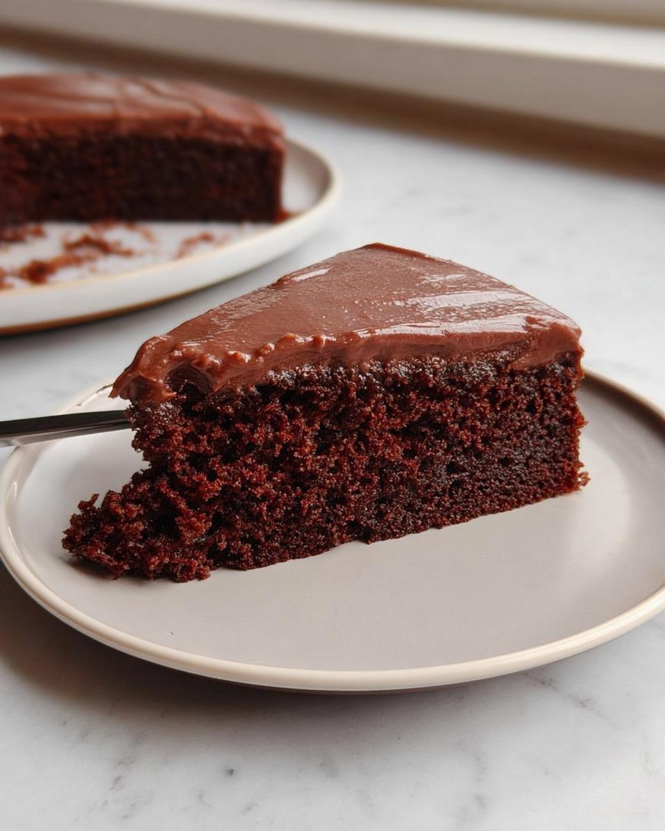 A rich, dark slice of Easy Snacking Sheet Cake topped with glossy chocolate frosting on a light gray plate.