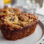Close-up of a perfectly baked Banana Bread Minis with a caramelized banana slice on top, resting on a white plate.