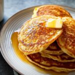 A close-up of a tall stack of golden brown Fluffy Buttermilk Pancakes topped with melting butter and syrup.