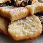 Close-up of various Gold-Dusted Shortbread cookies, some topped with sugar or crushed peppermint.
