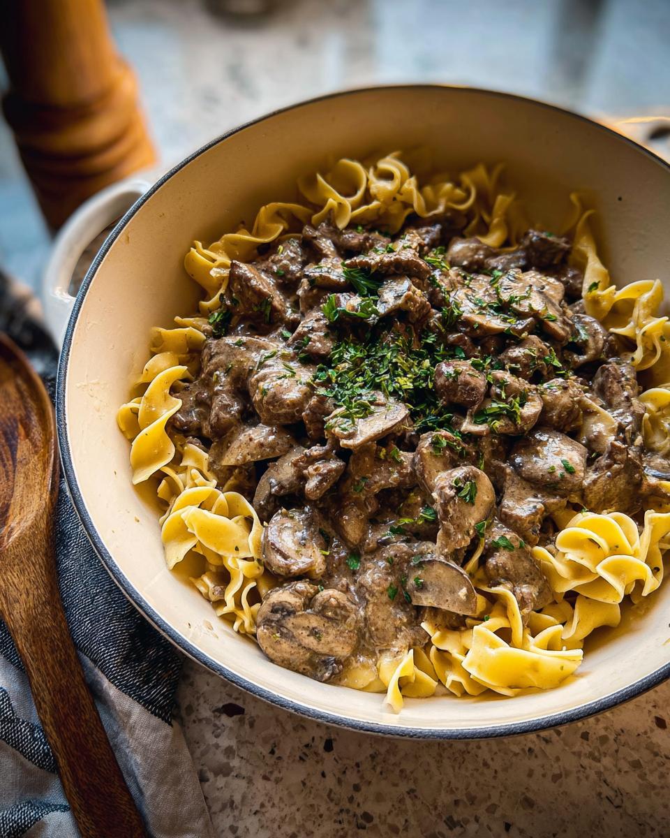 Close-up of rich Ground Beef Stroganoff served over wide egg noodles in a bowl, topped with fresh parsley.