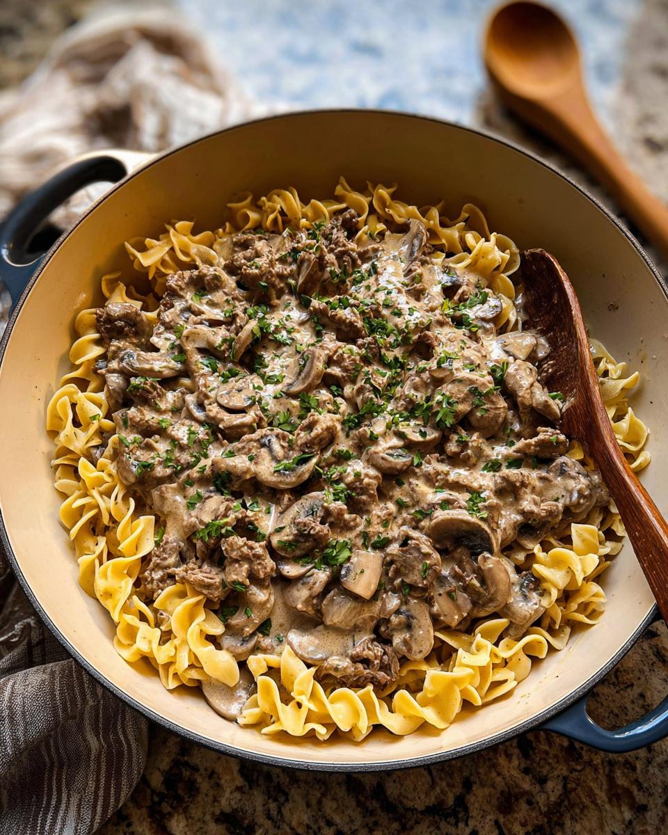 A skillet filled with creamy Ground Beef Stroganoff mixture served over wide egg noodles, garnished with parsley.