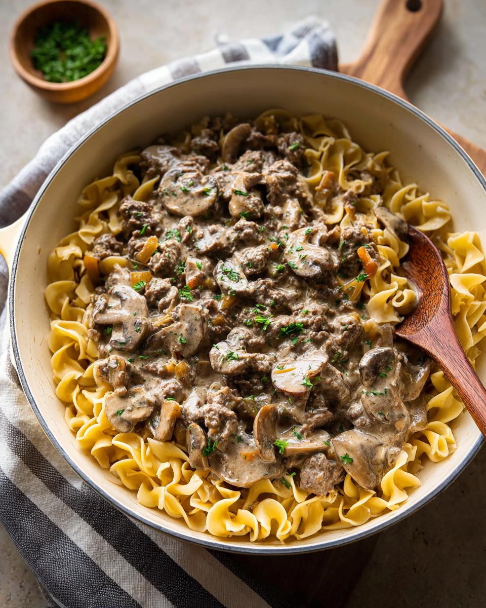 A skillet filled with creamy Ground Beef Stroganoff served over wide egg noodles, garnished with parsley.