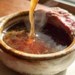 Hot Homemade Au Jus without drippings being poured into a rustic bowl containing a slice of roast beef.