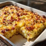 A freshly baked Loaded Breakfast Casserole with Bacon and Potatoes showing a slice removed, featuring golden cheese and crispy bacon.