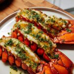 Three cooked lobster tails topped generously with garlic lemon butter and fresh parsley.