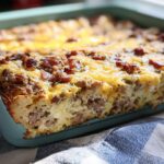 A close-up view of a freshly baked Make-Ahead Breakfast Strata with Bread & Cheese topped with melted cheddar and bacon bits.