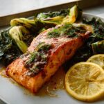 A glazed fillet of Maple Dijon Salmon Sheet Pan served with wilted greens and lemon slices.