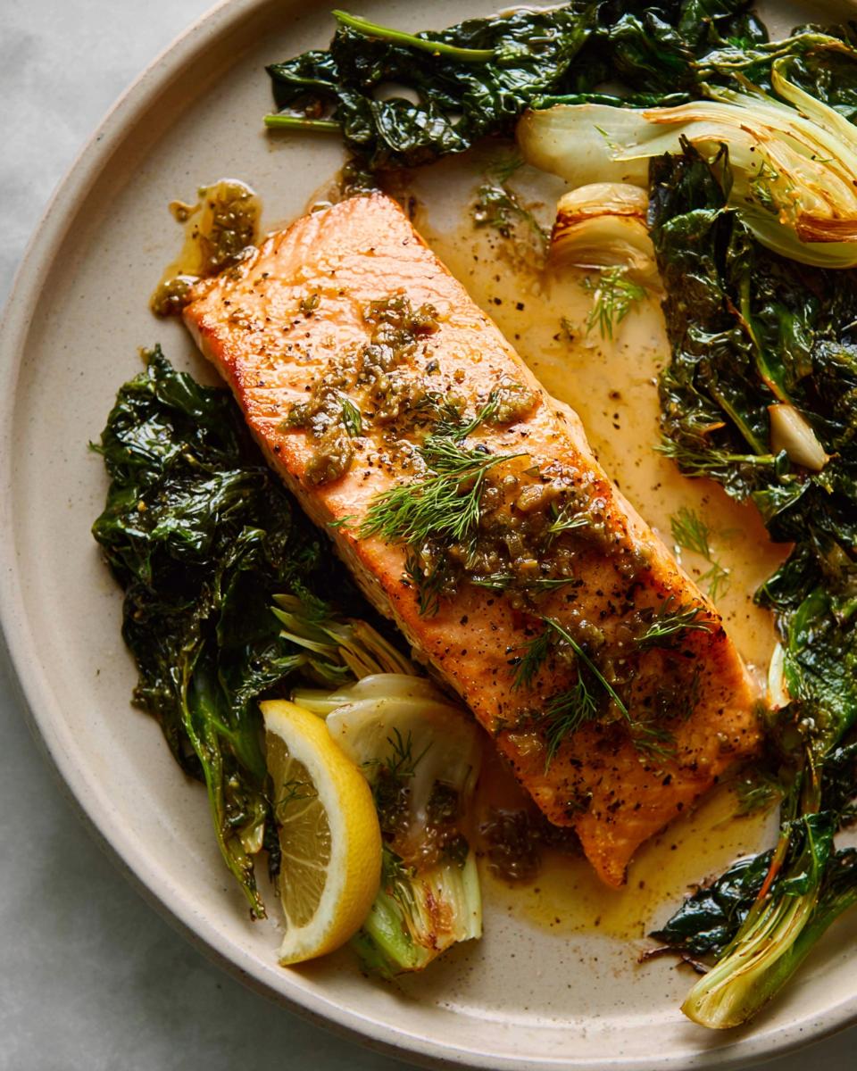 A cooked fillet of Maple Dijon Salmon Sheet Pan served on a plate with wilted greens and a lemon wedge.