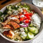 A vibrant bowl featuring sliced seasoned chicken over rice, topped with tzatziki, cucumbers, tomatoes, and feta for Mediterranean Chicken Bowls.