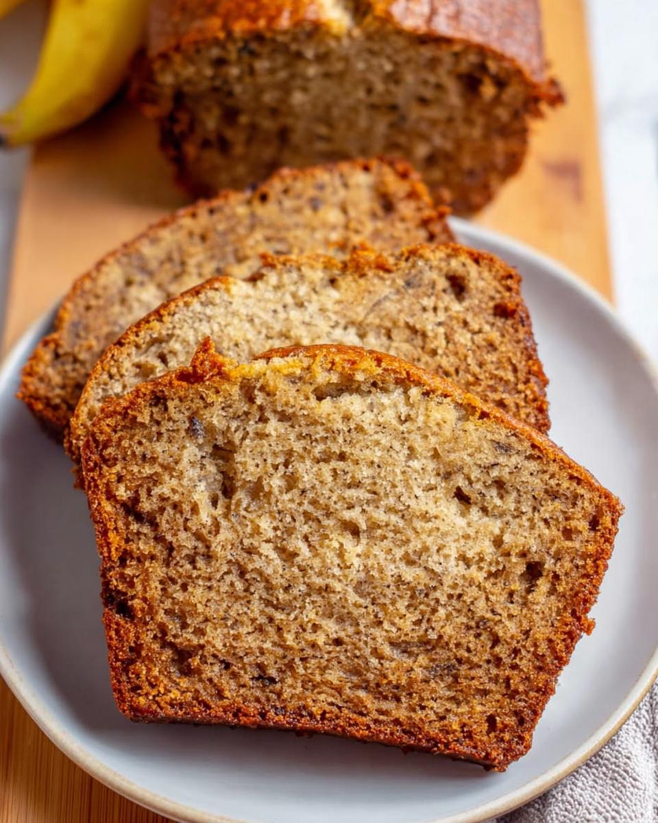 Close-up of moist slices of One Bowl Banana Bread served on a plate with the loaf in the background.