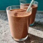Close-up of a rich, chocolate-brown Peanut Butter Protein Smoothie in a glass with a striped straw.