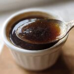 Close-up of a spoonful of rich, dark brown liquid from a small white ramekin, illustrating the perfect Au Jus recipe.