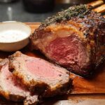 A perfectly cooked Perfect Prime Rib roast, sliced to show medium-rare center, served with a side of creamy sauce.